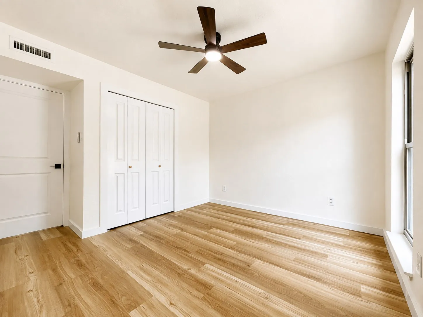Wood-finish flooring, white walls, ceiling fan with integrated lighting, and a window with a white sill