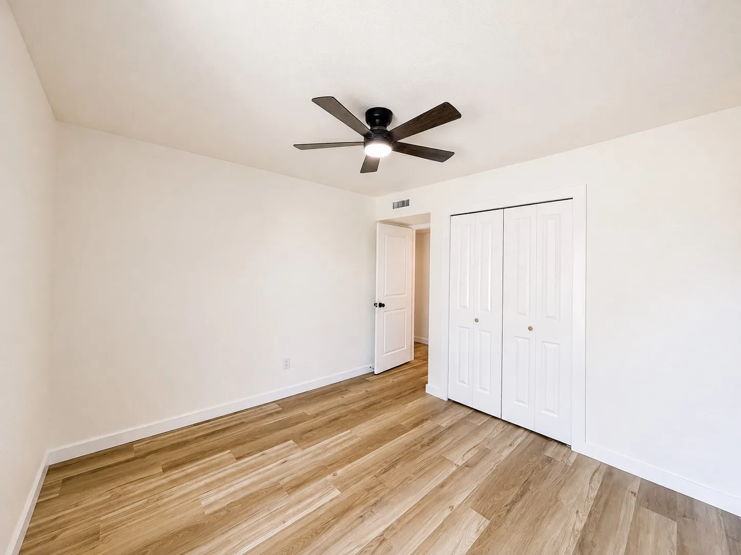 Wood-finish flooring, white walls, white trim, and a ceiling fan with integrated lighting