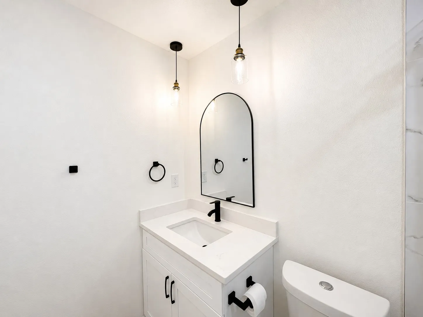 White vanity with a single basin sink, white countertop, and black fixtures