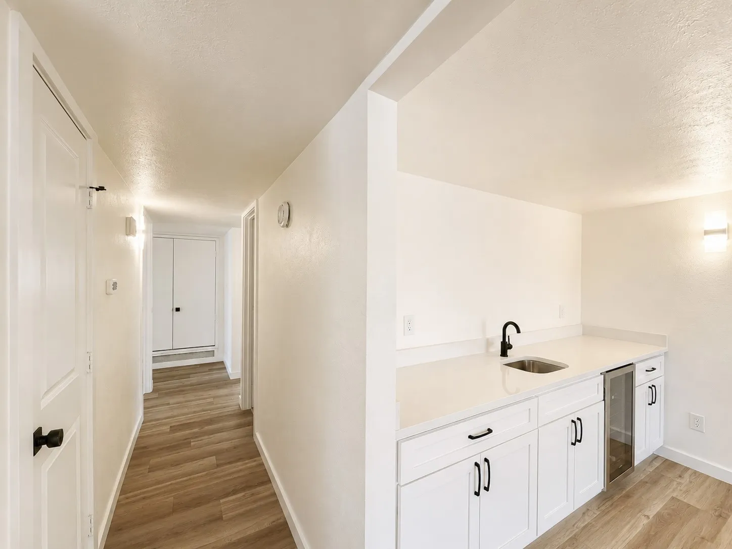 Hallway featuring wood-finish flooring, white doors with black hardware, and wall-mounted sconces