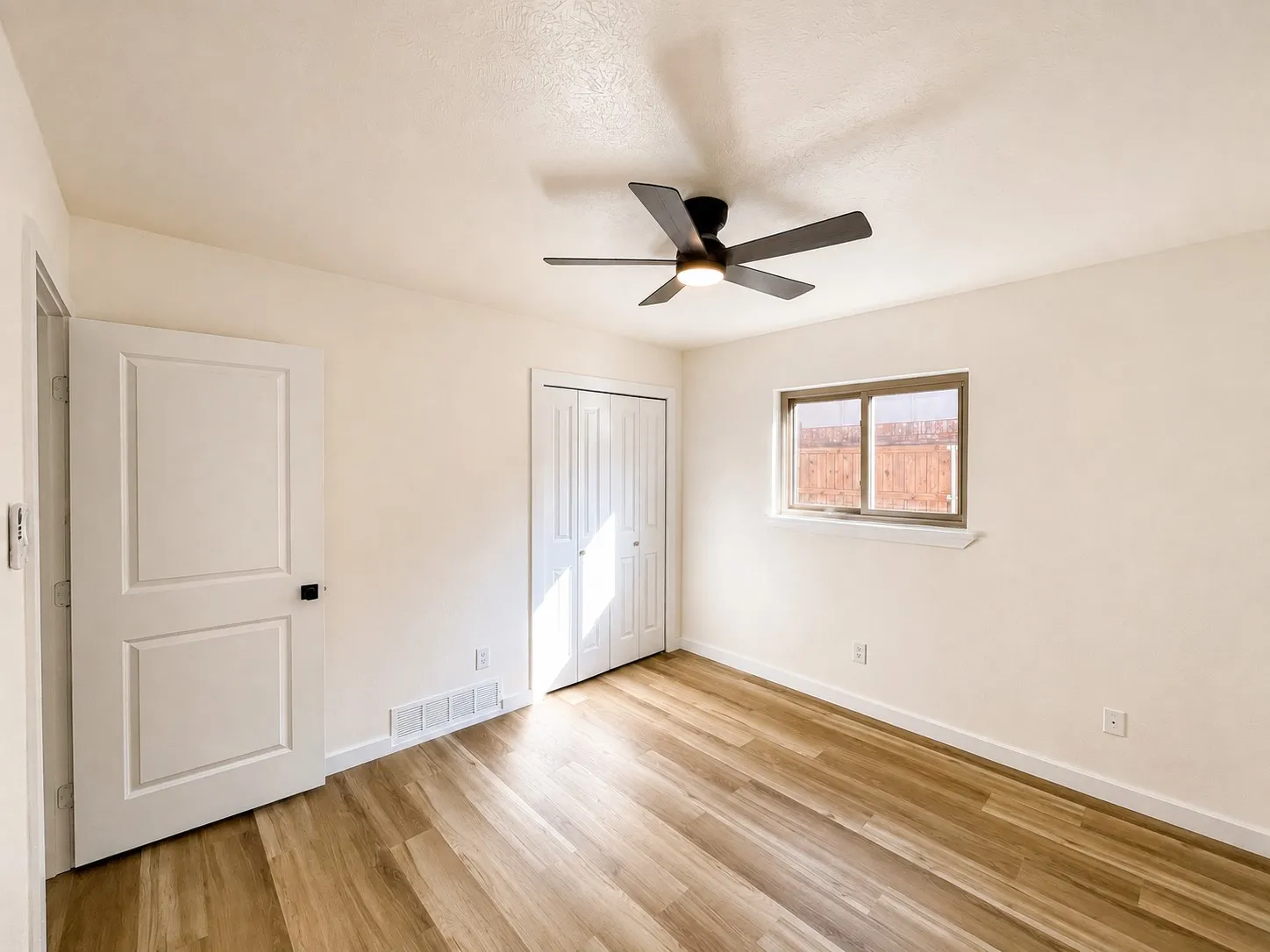 Wood-finish flooring, white paneled doors, ceiling fan with integrated lighting, and a window with a sill