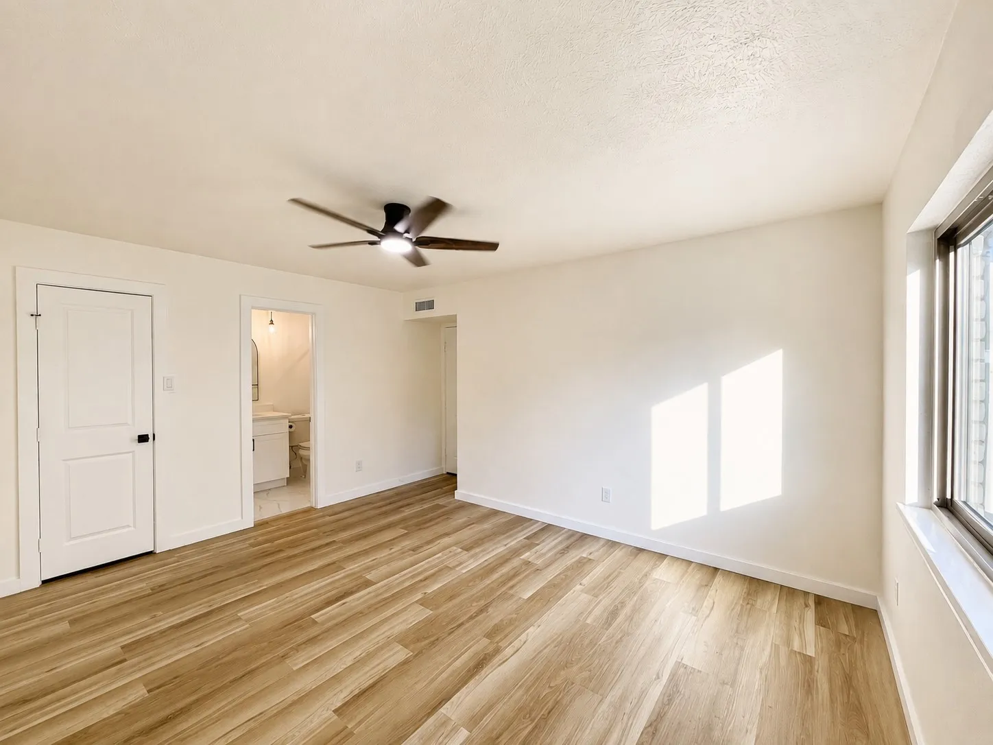 Wood-finish flooring, ceiling fan, white paneled door, and large window
