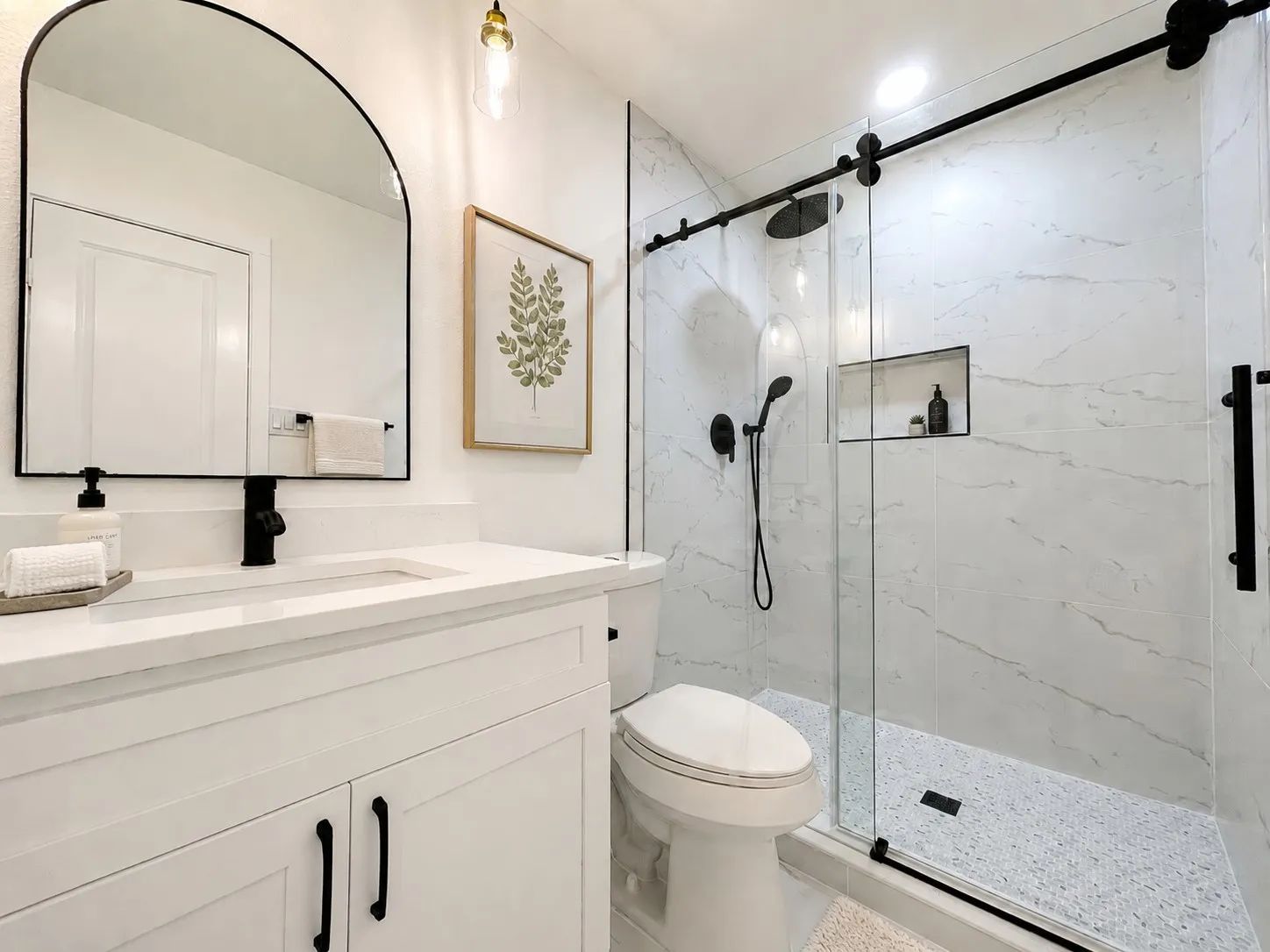 White vanity with integrated sink, black faucet, and arched mirror
