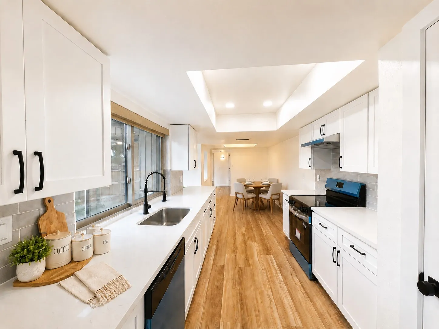 White shaker cabinetry, light-toned countertops, subway tile backsplash, wood-finish flooring, and a skylight