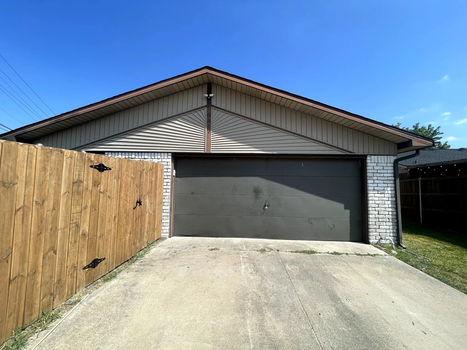 Attached garage with a paved driveway, white brick siding, horizontal siding, and a wooden fence