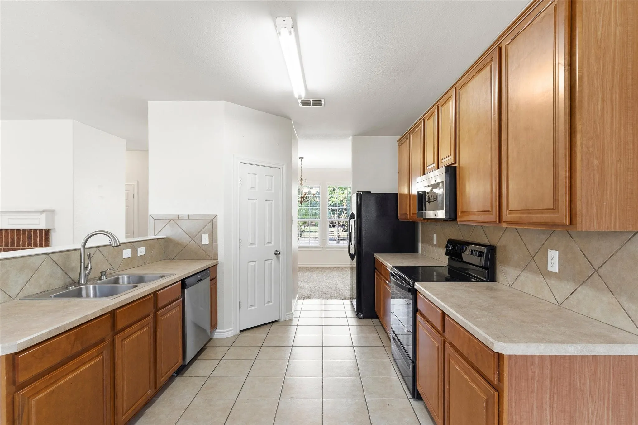 Kitchen featuring wood-finish cabinetry, tile flooring, stone-look countertops, and a stainless steel double basin sink