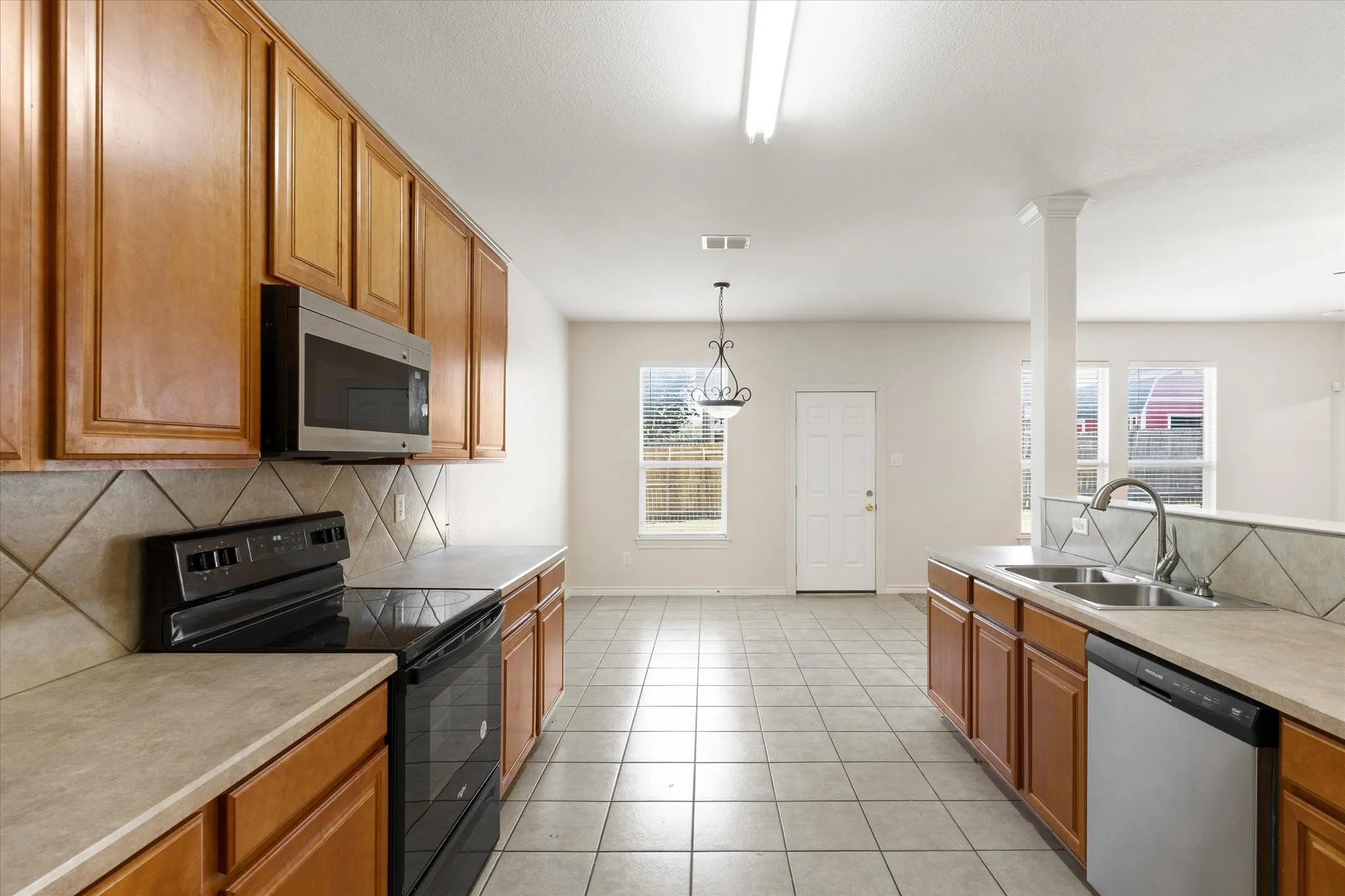 Kitchen featuring wood cabinetry, stainless steel microwave, black electric range, and tile flooring