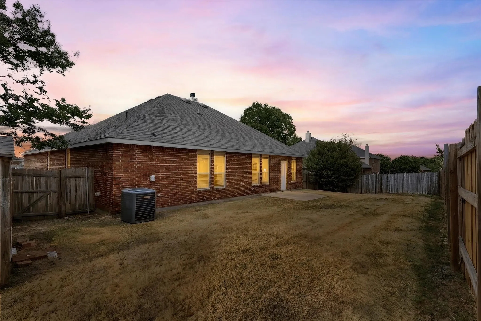 Brick exterior, shingle roof, privacy fencing, concrete patio, and mature landscaping