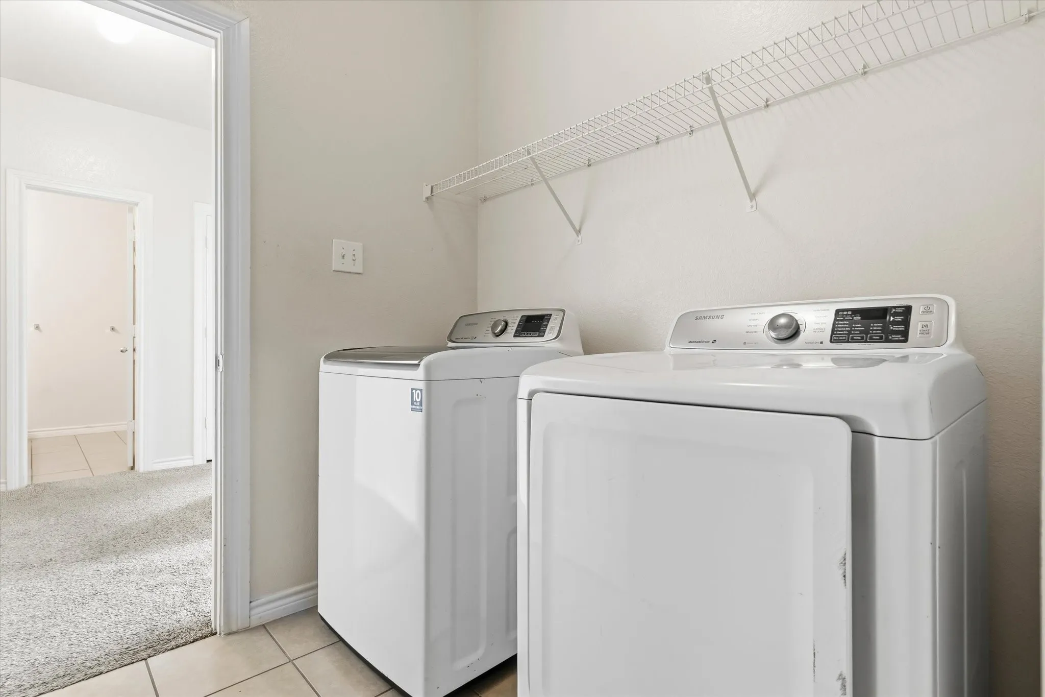Dedicated laundry area featuring tile flooring, neutral wall paint, and built-in wire shelving
