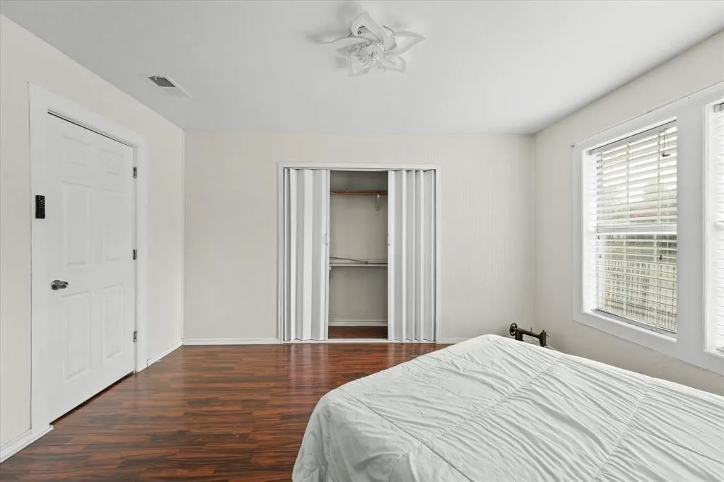 Wood-finish flooring, white paneled door, bi-fold closet doors with shelving, white window blinds, and a decorative ceiling fan