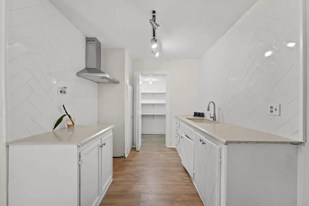 Galley kitchen featuring wood-finish flooring, white cabinetry, light-toned countertops, and a stainless steel range hood