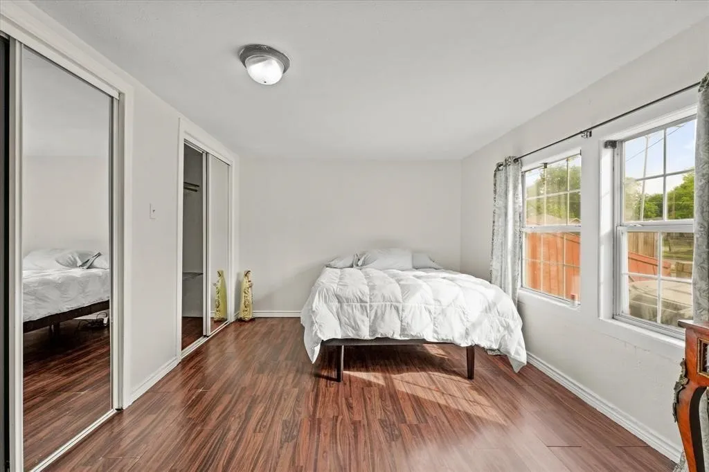 Wood-finish flooring, two large windows, overhead flush-mount lighting, and two mirrored sliding door closets