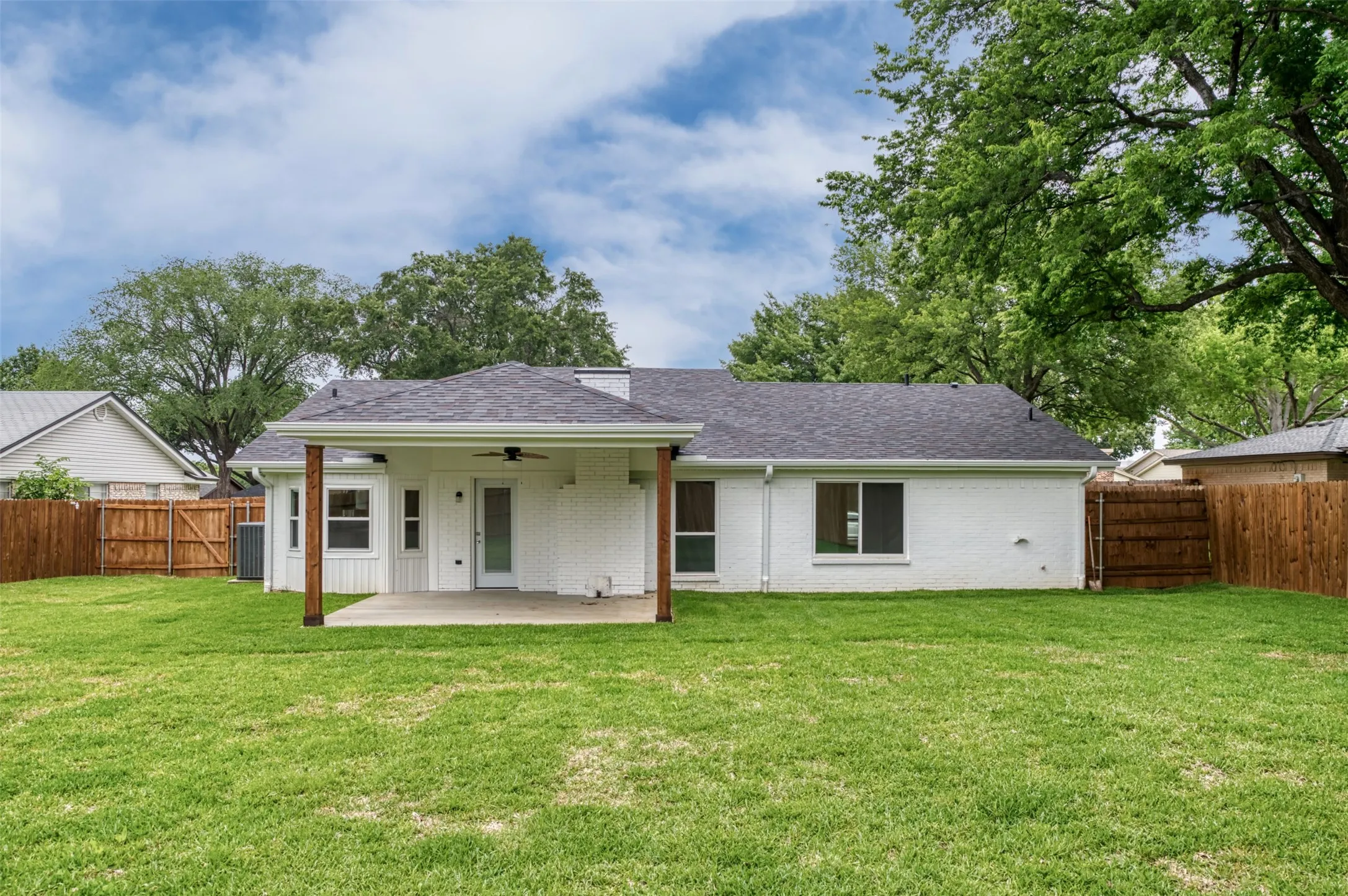 Expansive backyard featuring a covered patio, concrete slab, wood privacy fencing, and a white painted brick exterior