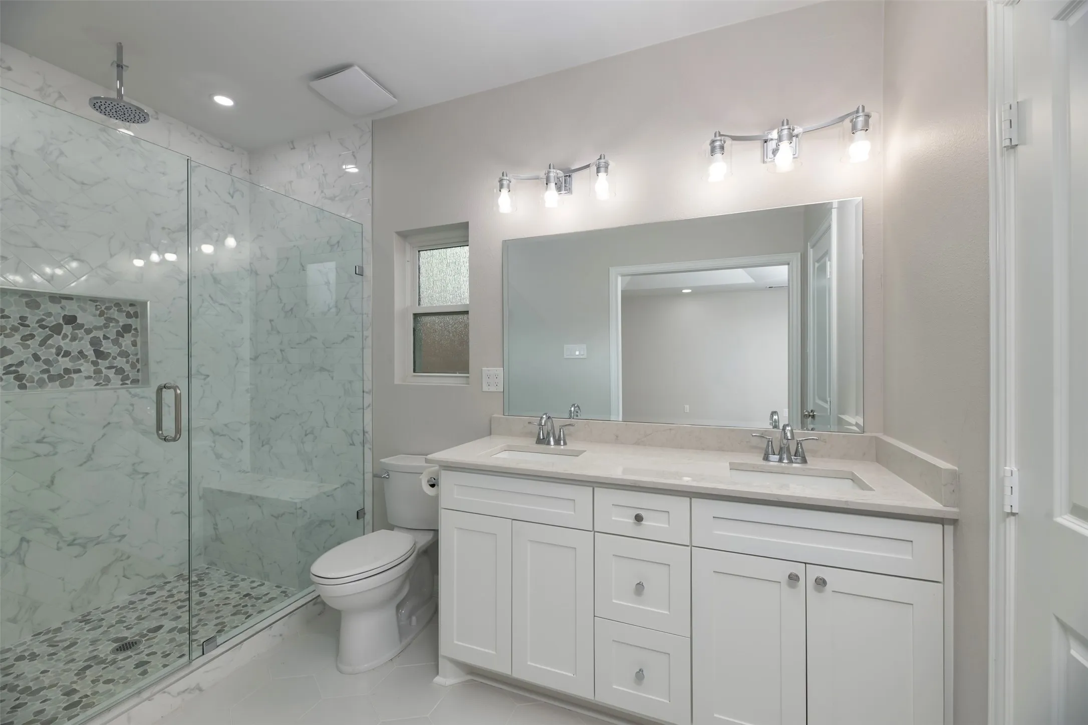 Dual vanity with white cabinetry, a spacious mirror, and overhead lighting