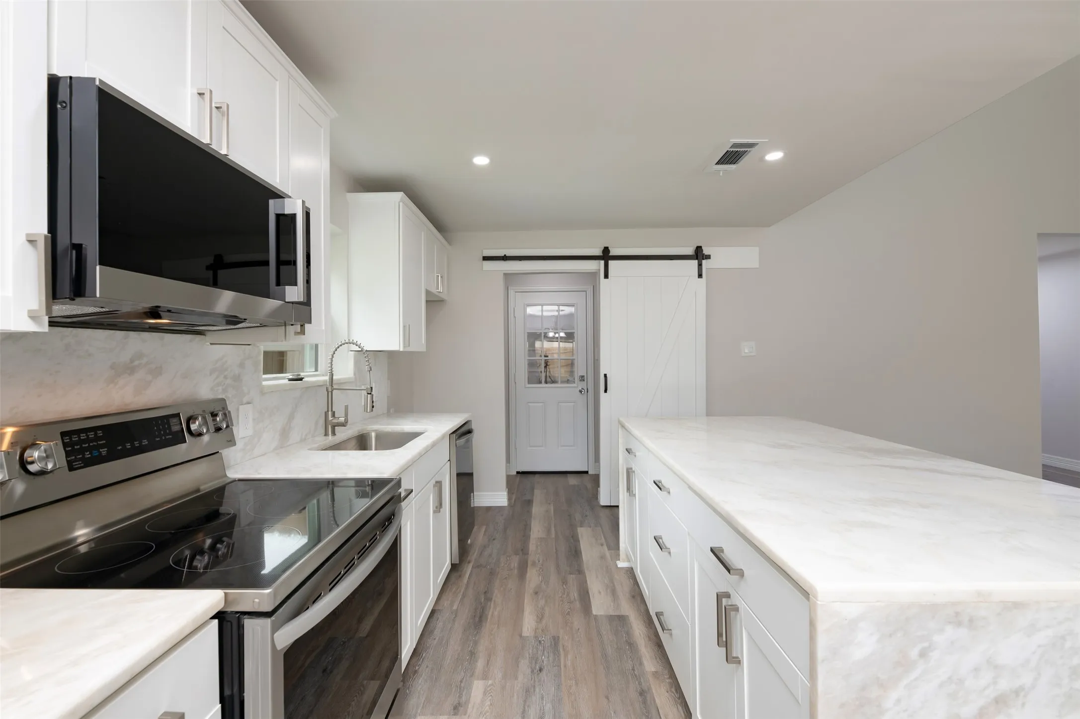 Kitchen featuring white shaker cabinetry, stainless steel appliances, a large center island, wood-finish flooring, and a white barn door