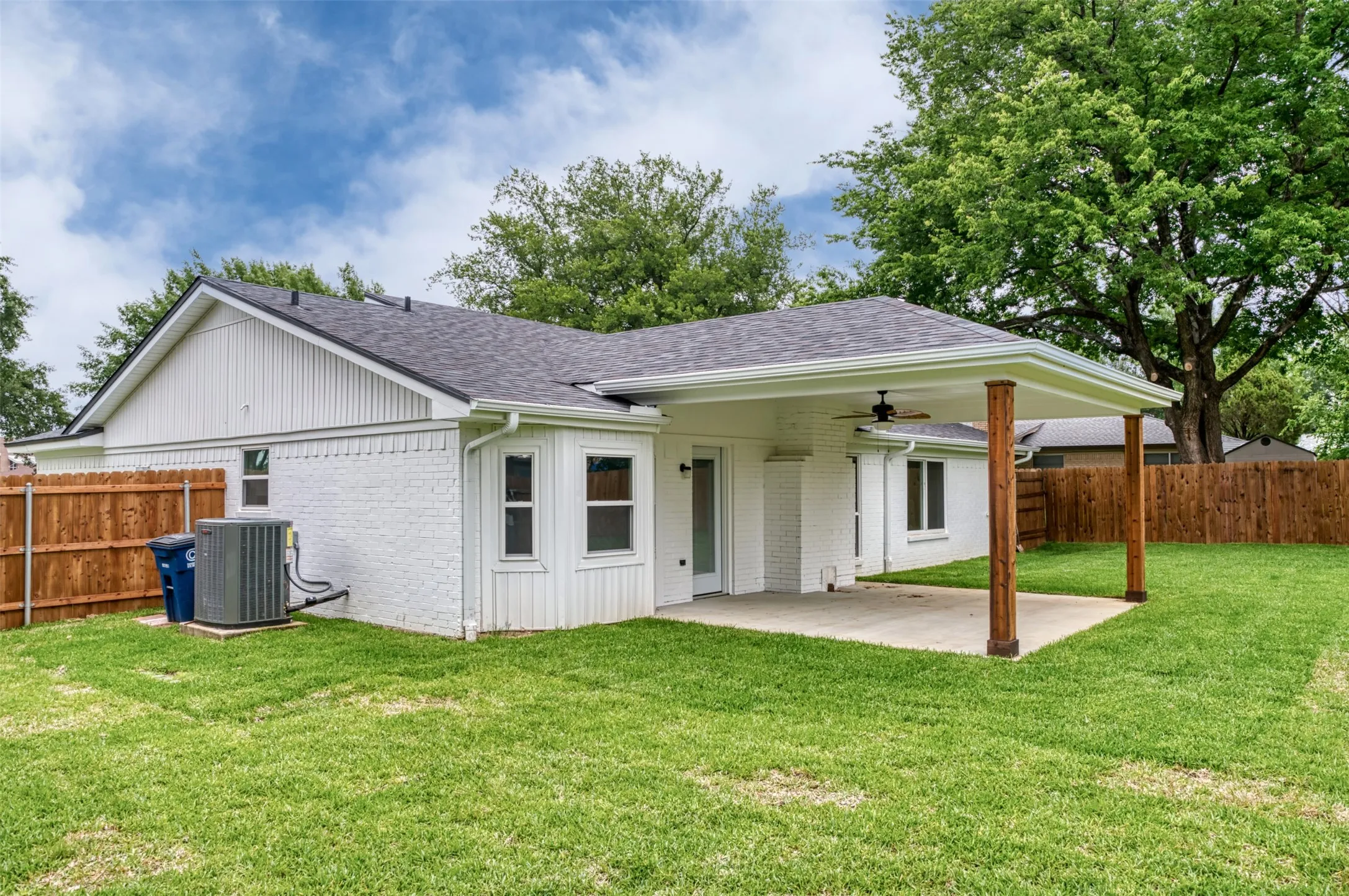 Covered patio with a ceiling fan, concrete patio surface, white painted brick exterior, and a wood privacy fence