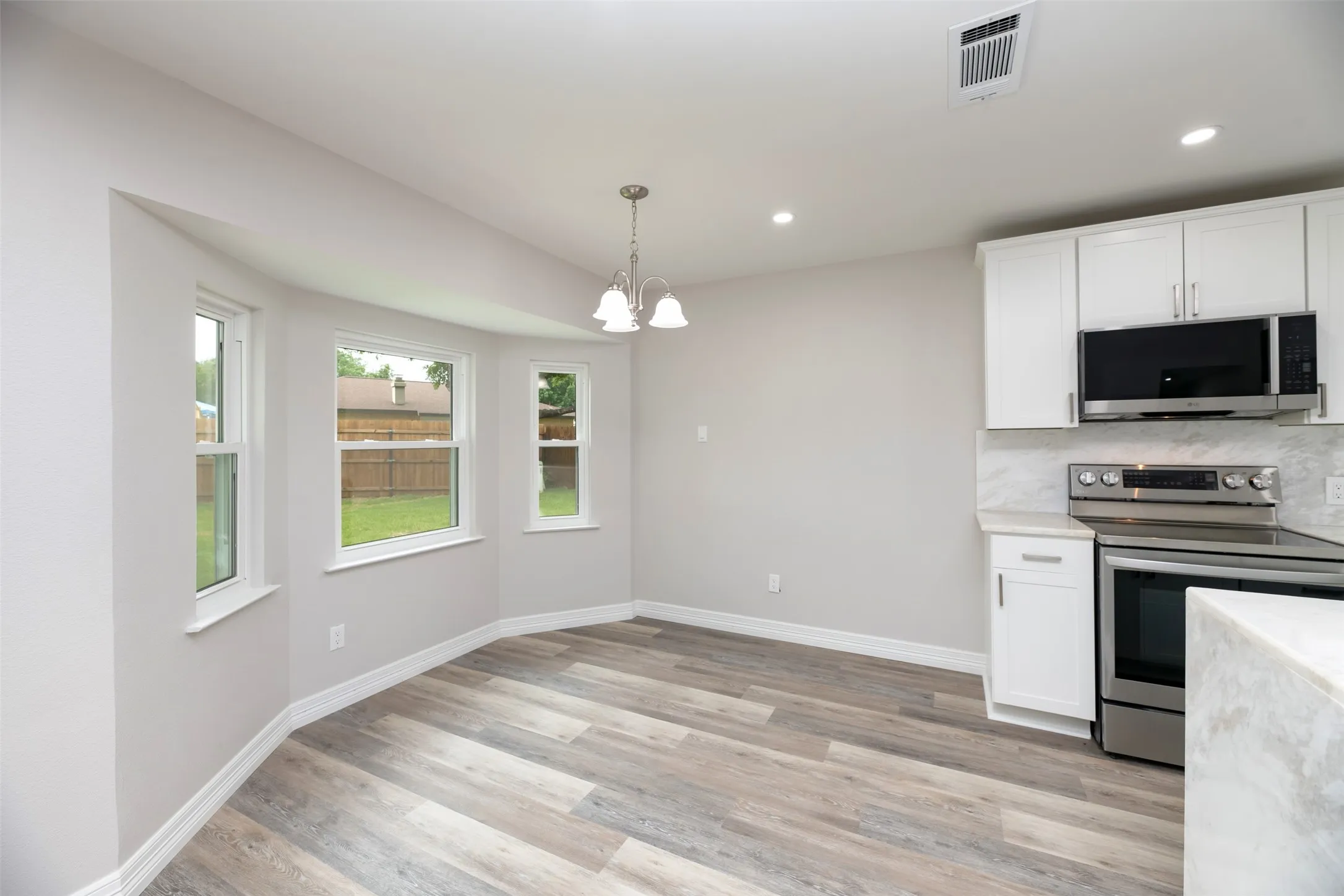 White shaker cabinetry, stainless steel appliances, wood-finish flooring, recessed lighting, and a bay window