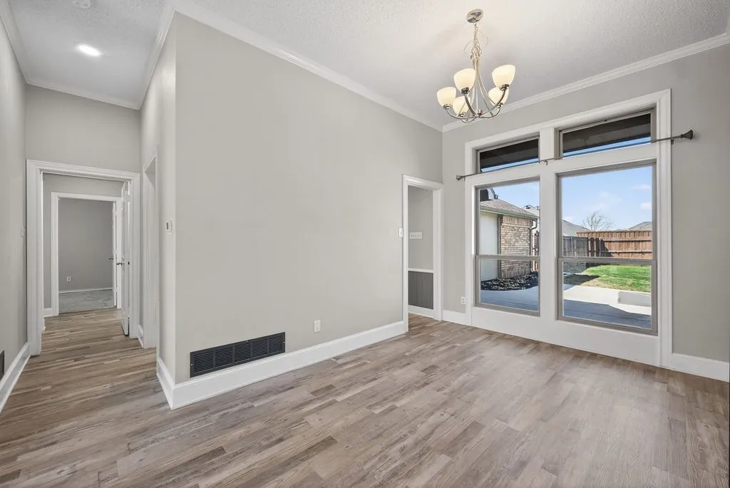 Unfurnished dining area with crown molding, a textured ceiling, hanging lights, and light wood finished floors