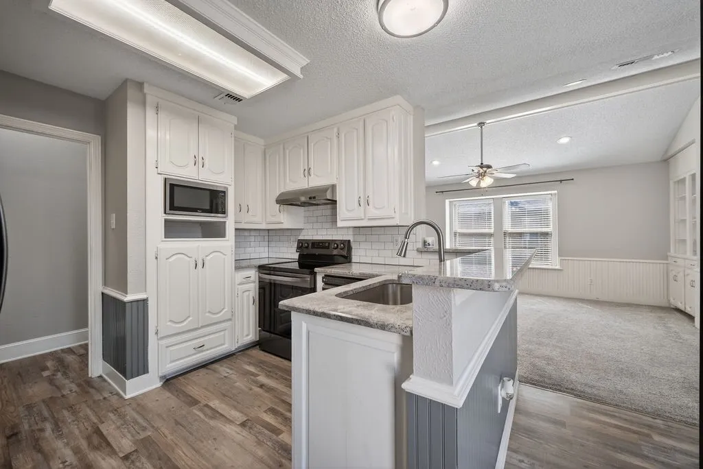 Kitchen featuring stainless steel appliances, a peninsula, light stone countertops, a wainscoted wall, and ceiling fan