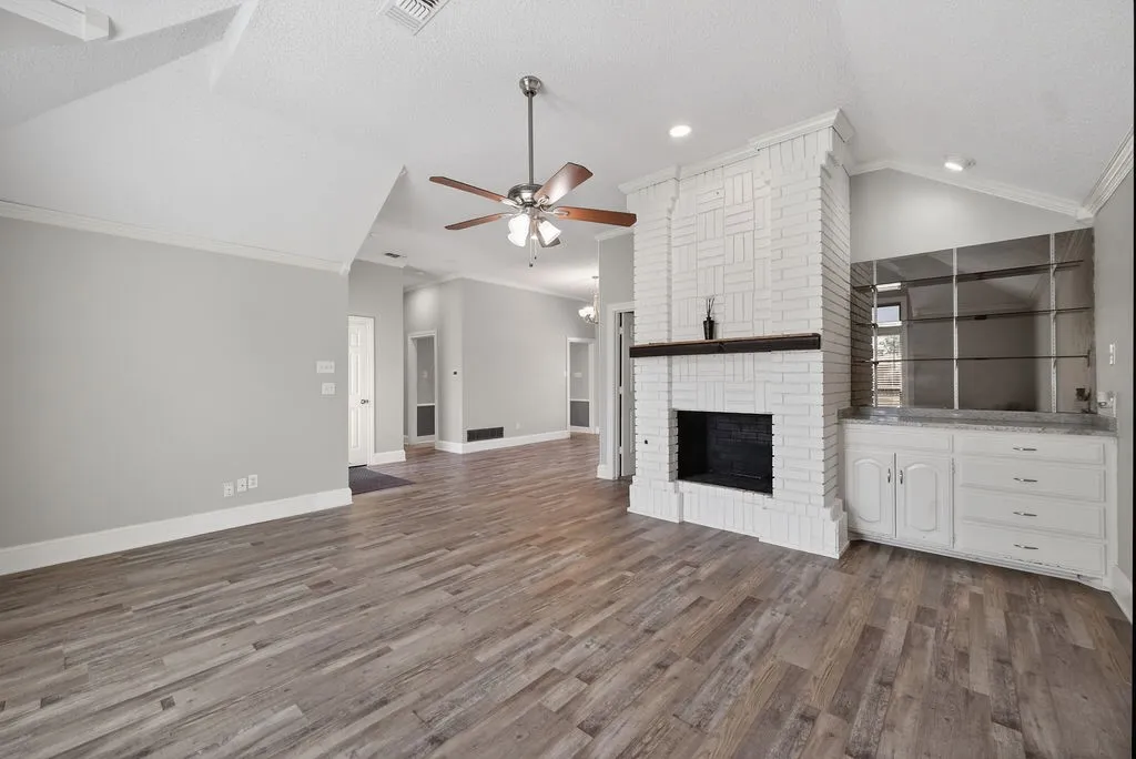 Unfurnished living room featuring crown molding, ceiling fan, a fireplace, dark wood-style floors, and recessed lighting