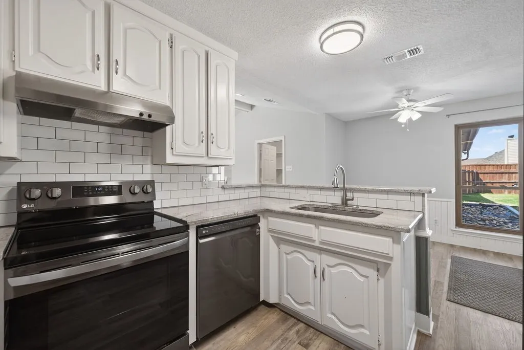 Kitchen with electric range, light stone counters, white cabinetry, a peninsula, and wainscoting