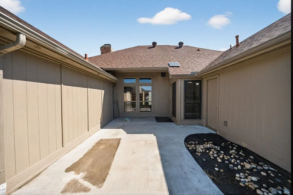 View of exterior entry with a chimney, a patio area, and a shingled roof