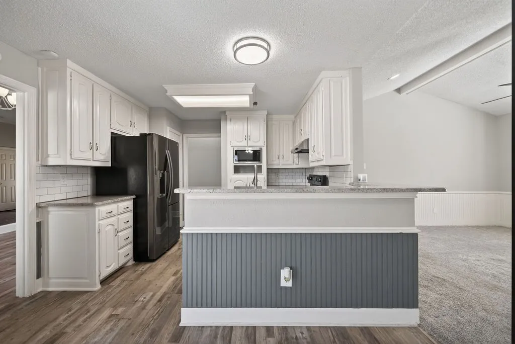 Kitchen with white cabinets, decorative backsplash, a peninsula, beam ceiling, and light stone counters