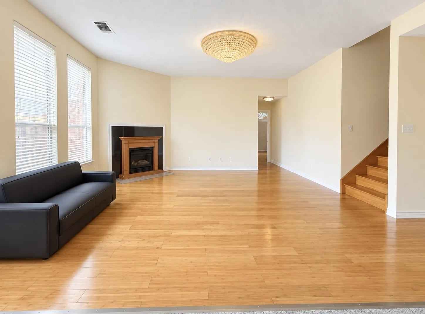 Spacious living area featuring wood-finish flooring, a traditional fireplace with a dark surround, multiple windows with horizontal blinds, and a contemporary beaded chandelier
