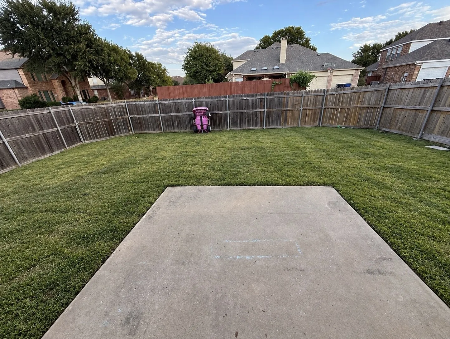 Expansive yard featuring a concrete patio, wood privacy fencing, and a large grass area