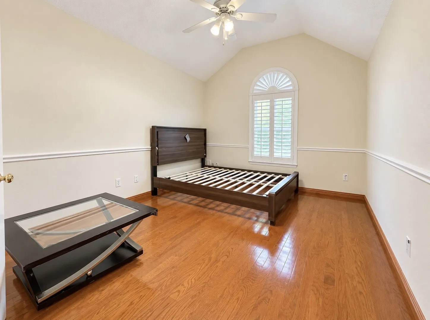 Vaulted ceiling with a ceiling fan, arched window with plantation shutters, wood-finish flooring, and chair rail molding