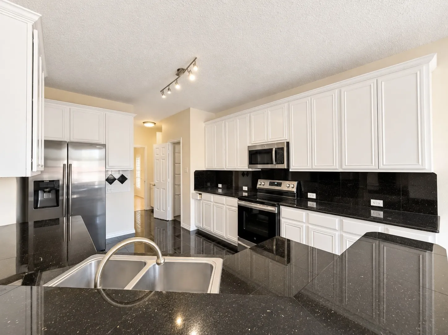 Kitchen featuring white upper and lower cabinetry, dark stone-finish countertops, stainless steel appliances, and a double basin sink