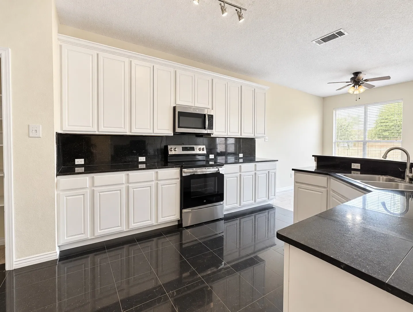 Kitchen featuring black tile flooring, white cabinetry, black countertops, and stainless steel appliances