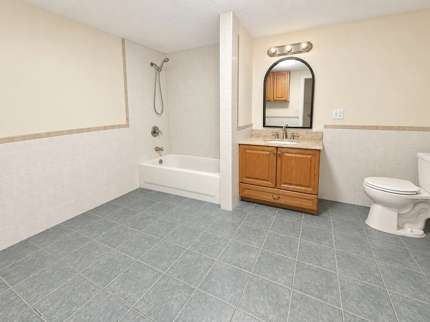 Bathroom featuring a full-size bathtub with shower, wood-finish vanity with countertop, and floor-to-ceiling wall tiling