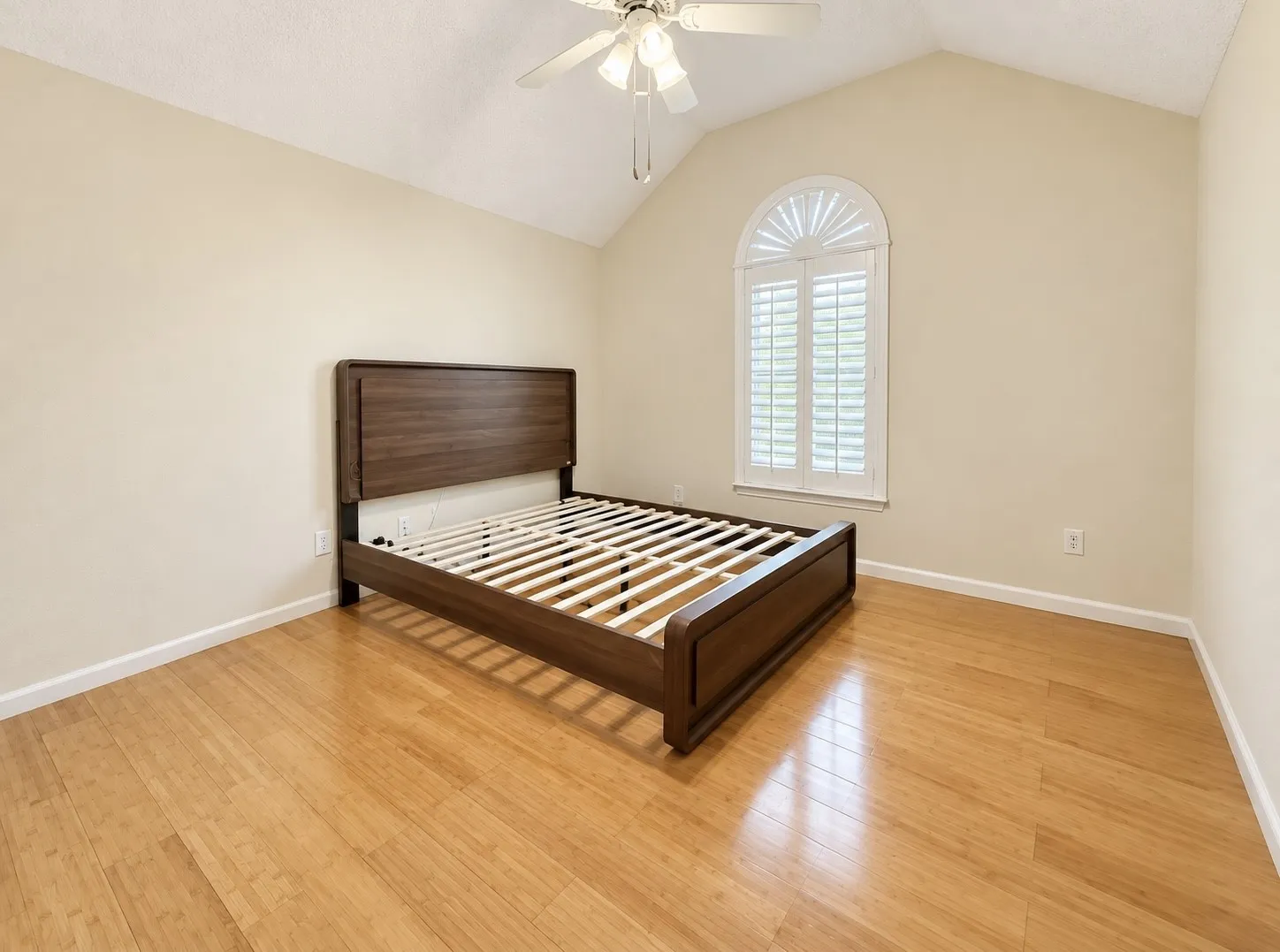 Vaulted ceiling with a ceiling fan, arched window with plantation shutters, light-toned wall paint, and wood-finish flooring