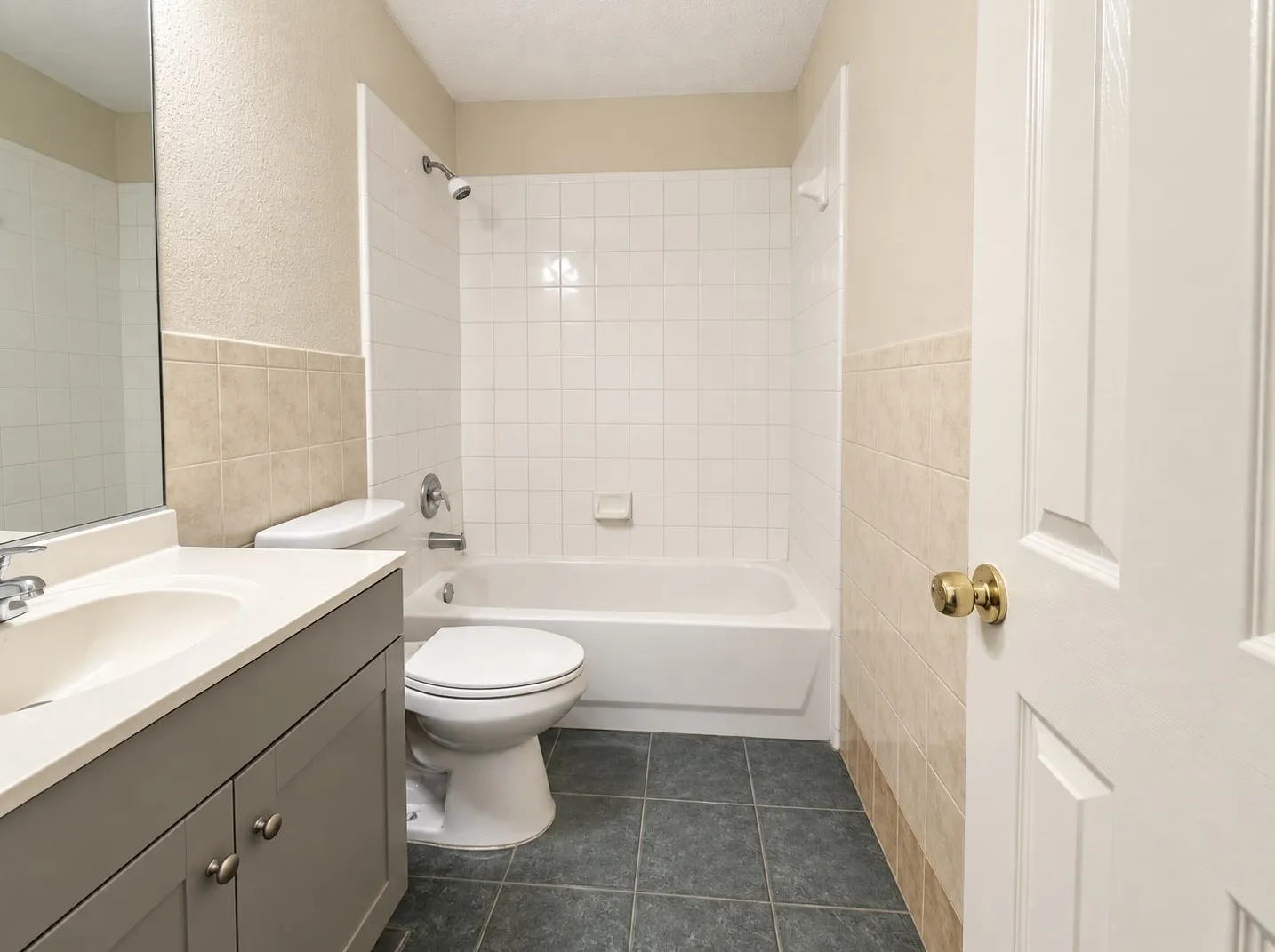 Bathroom featuring a vanity with an integrated sink, a white bathtub with a shower, a toilet, and dark tile flooring