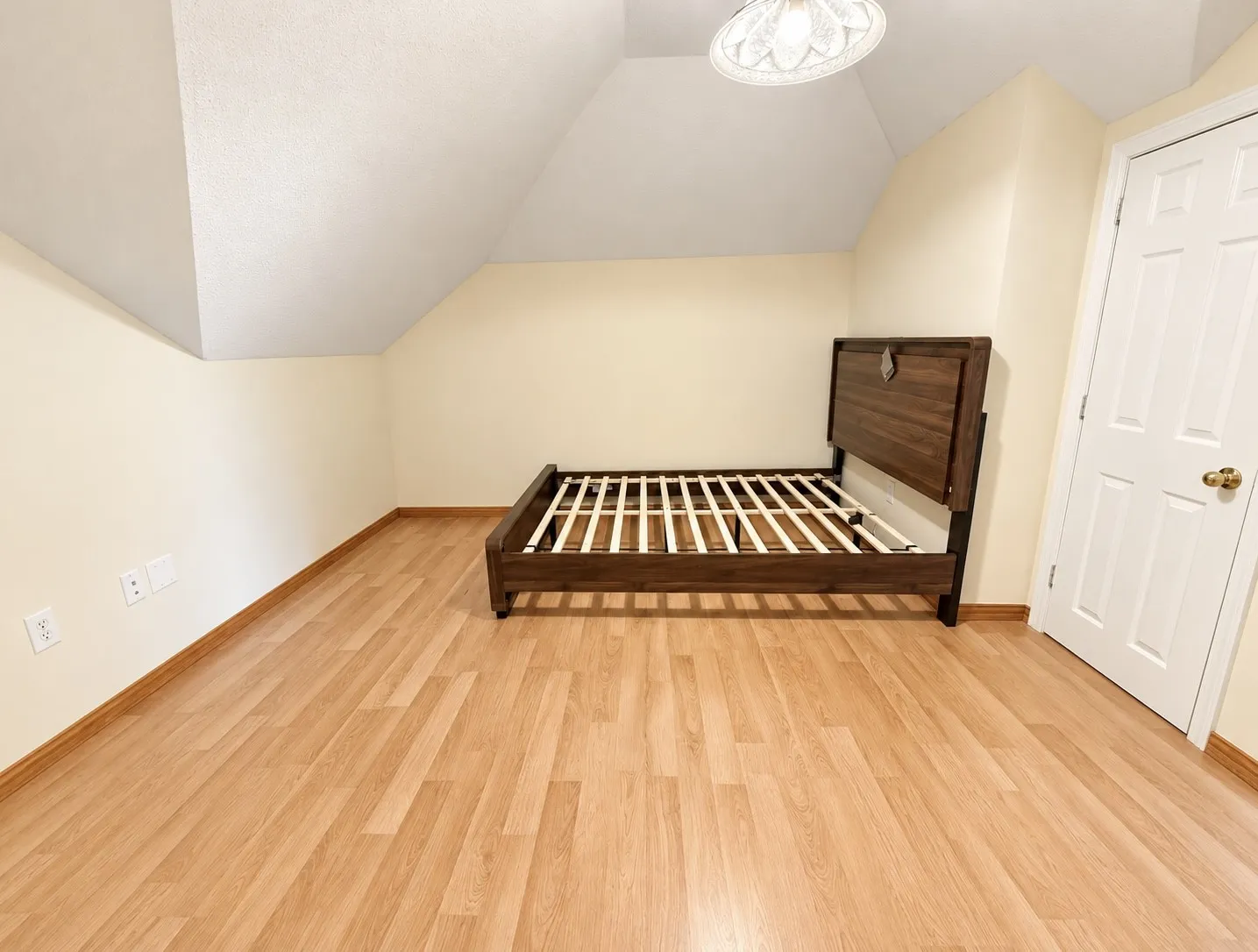 Vaulted ceiling with a flush-mount light fixture, wood-finish flooring, and a white interior door
