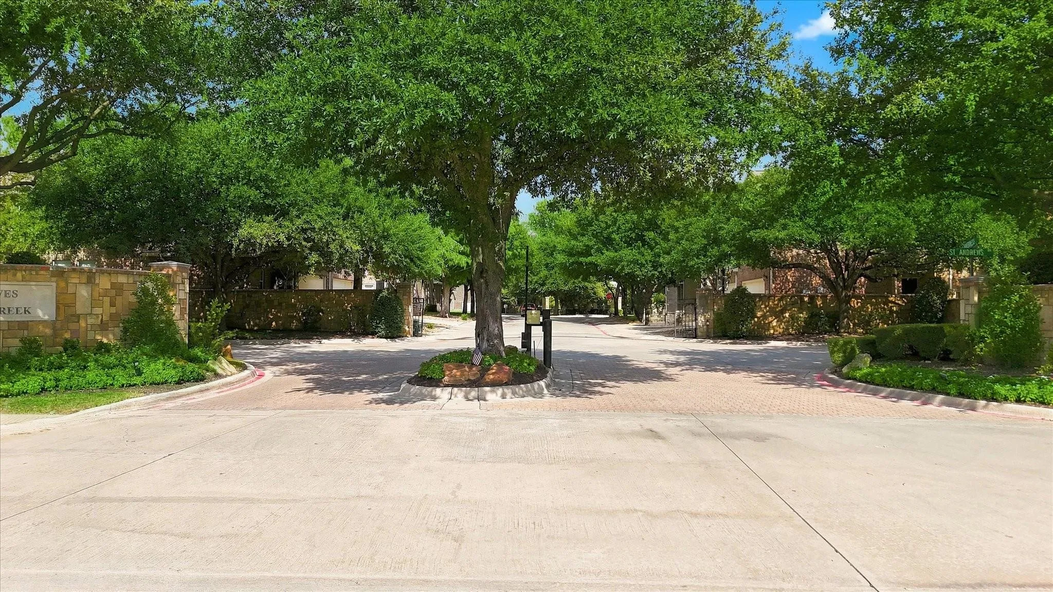 Paver stone roadway entrance framed by mature trees and stone retaining walls