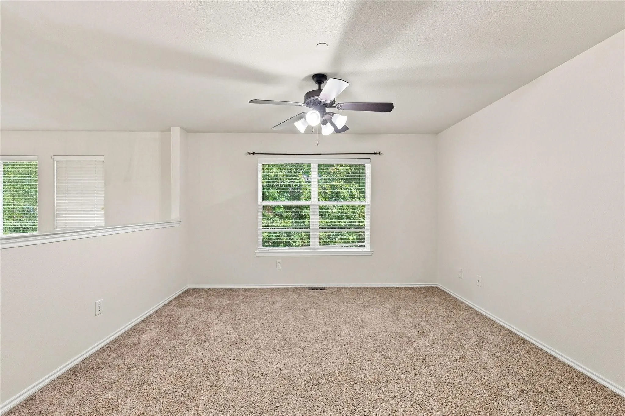 Neutral-toned carpeting, white walls, multiple windows with blinds, and a ceiling fan with integrated lighting
