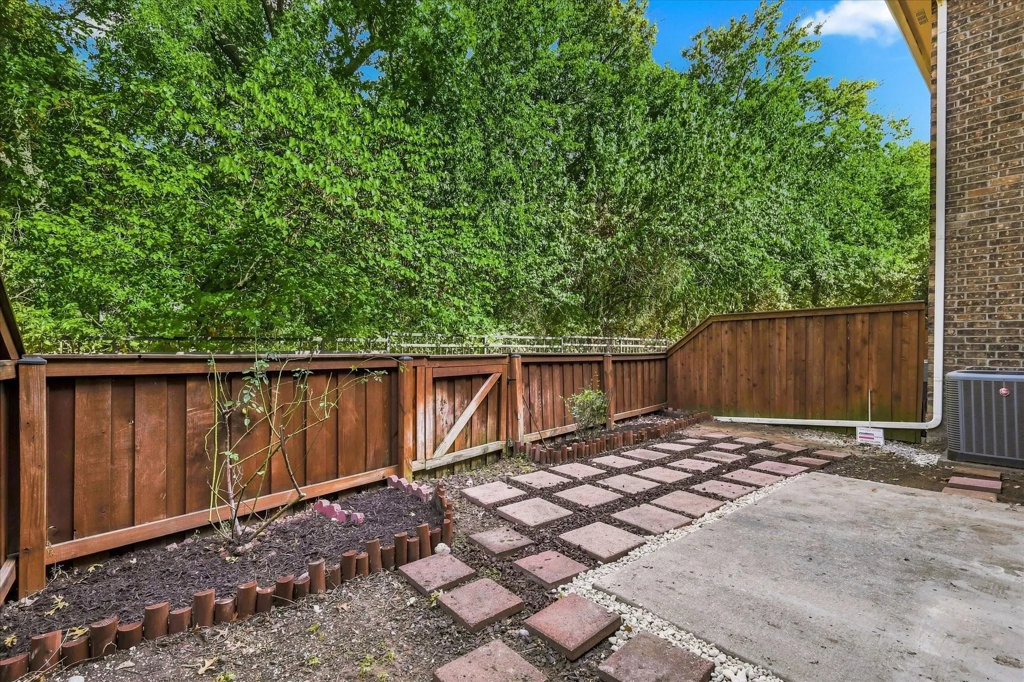 Private fenced area featuring a paver walkway, planting bed with edging, and a concrete patio
