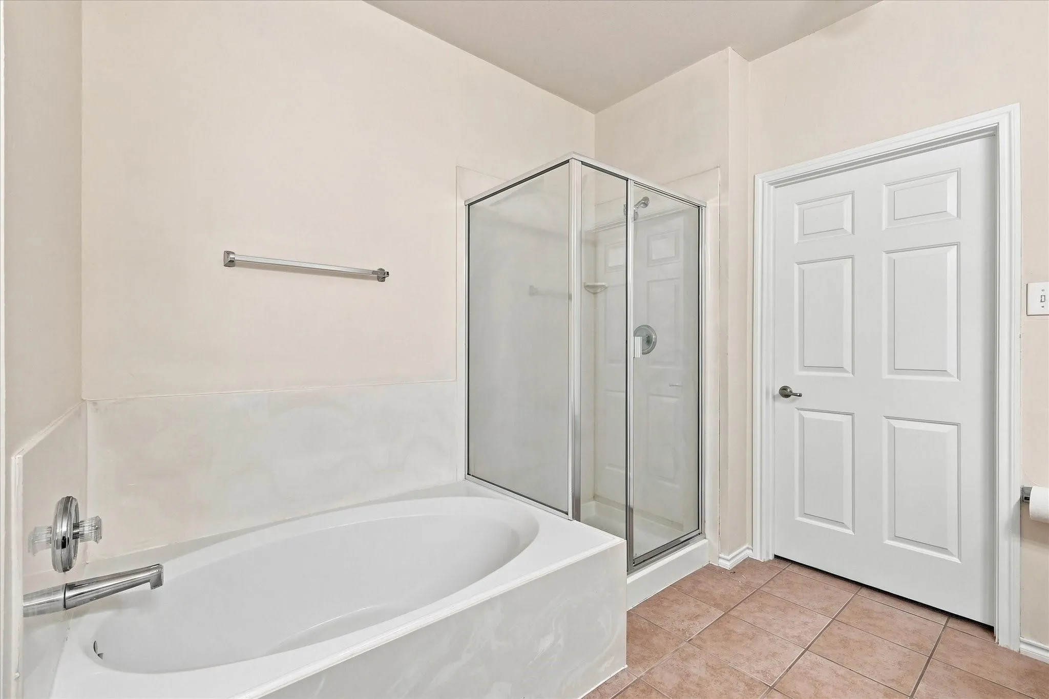 White soaking tub with deck-mounted chrome faucet, glass-enclosed shower with chrome fixtures, and tiled flooring