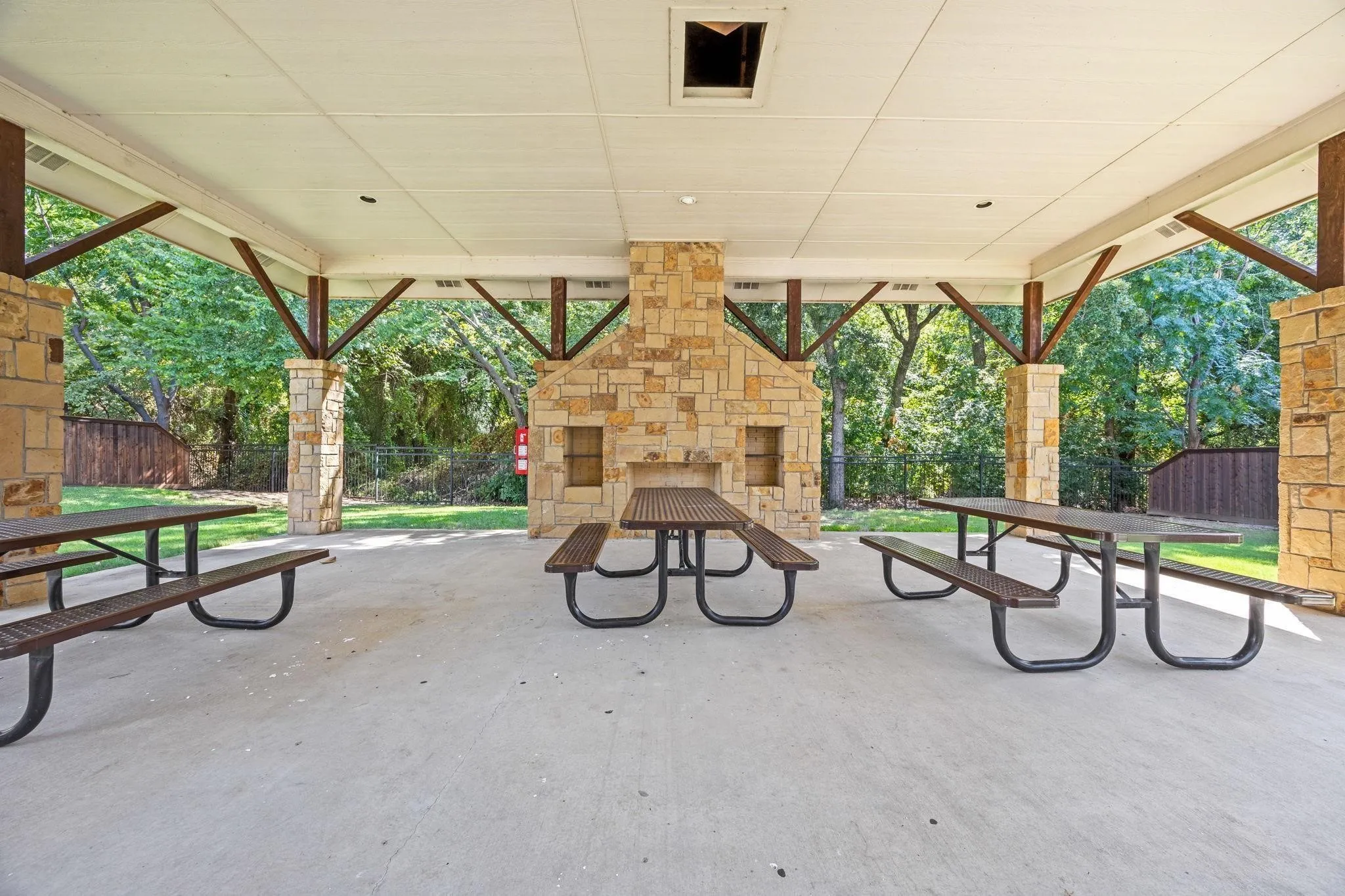 Covered patio featuring a stone-clad fireplace, stone support columns, and exposed wood beam accents