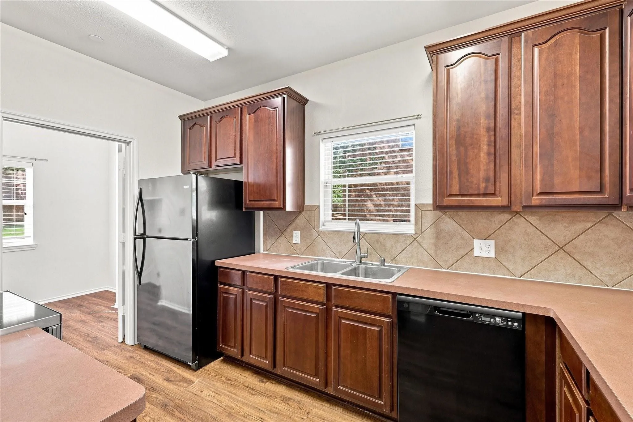 Kitchen featuring wood-finish flooring, wood cabinetry, stainless steel refrigerator, black dishwasher, and tile backsplash