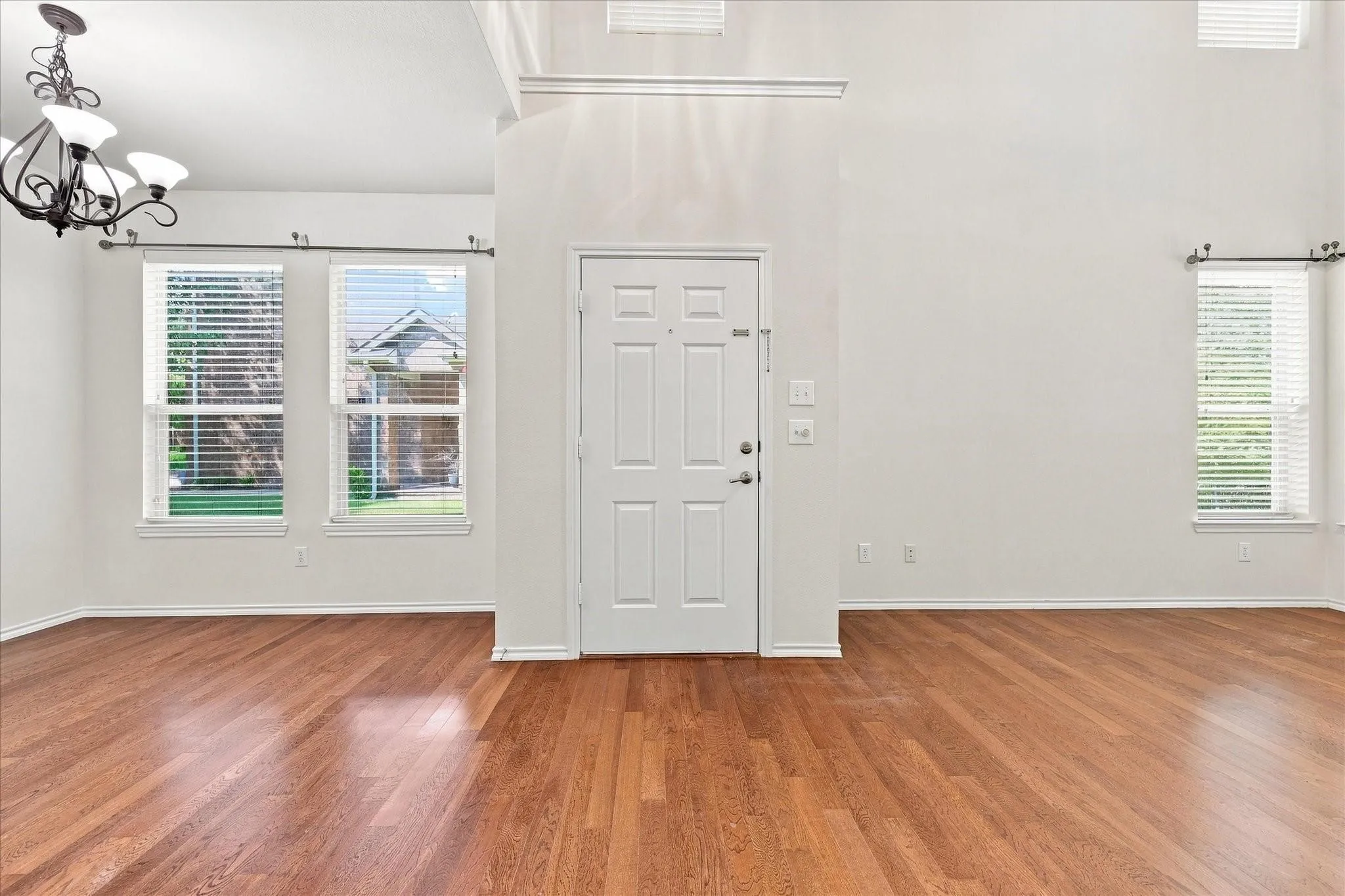 Vaulted ceiling with decorative chandelier, wood-finish flooring, white paneled door, and multiple windows