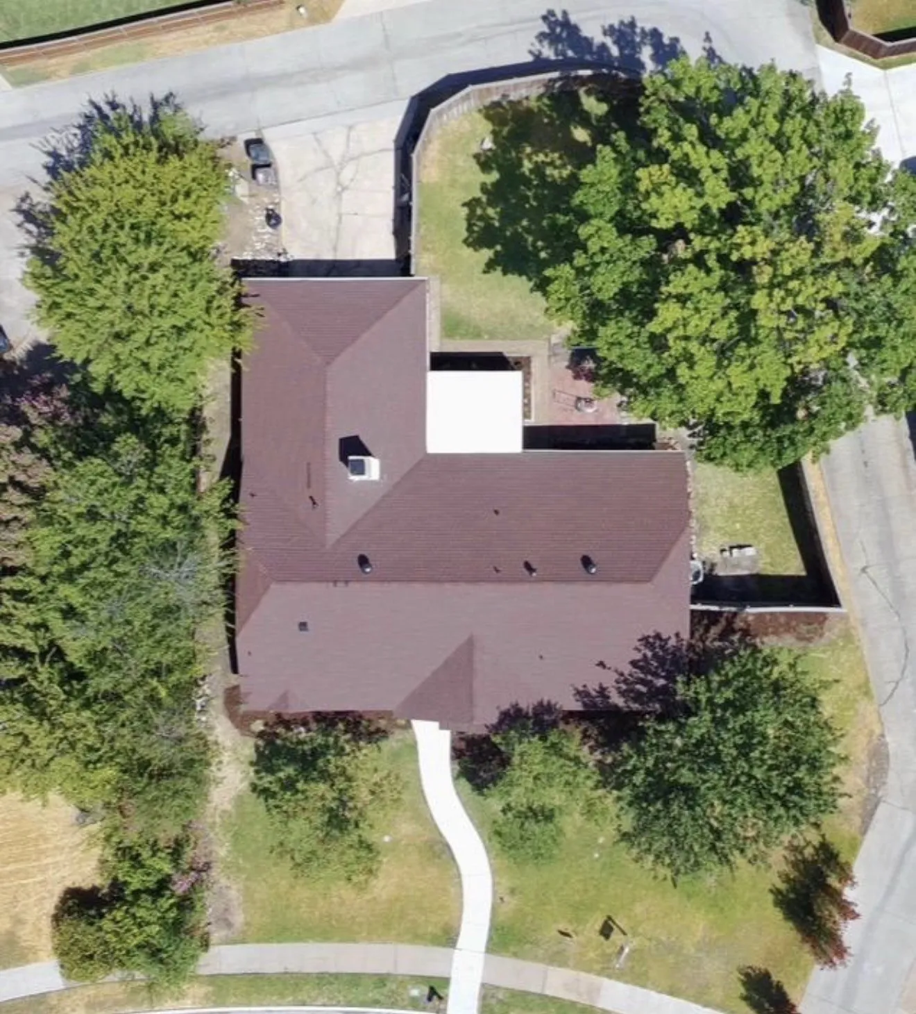 Brown shingle roof with multiple gables, extensive paved driveway, mature trees, manicured front lawn, and paved front walkway
