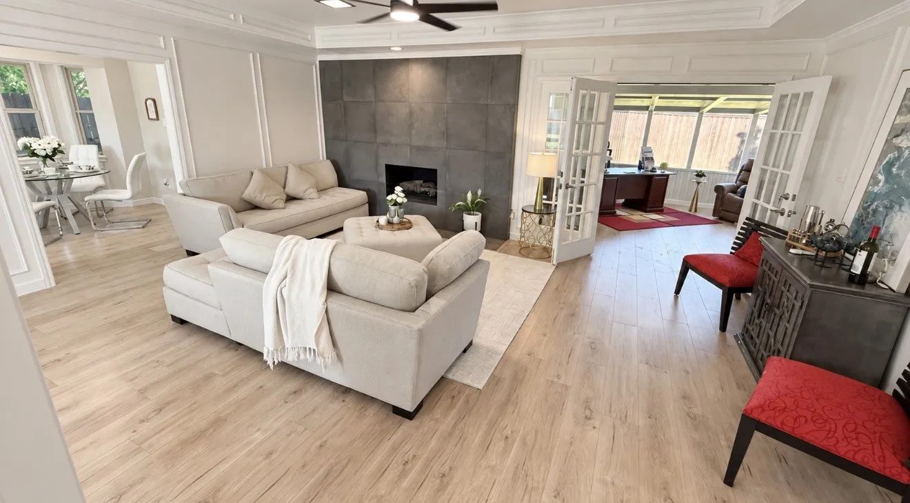 Laminate-finish flooring throughout, tray ceiling with fan, built-in fireplace with dark tile accent wall, wall paneling, and French doors