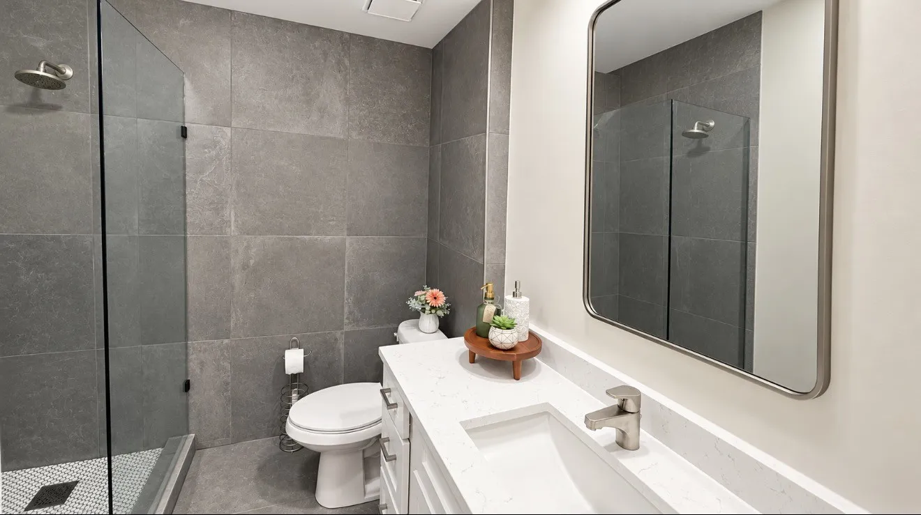 Glass-enclosed shower with a rain showerhead, grey large-format tile walls, white vanity with an integrated sink.