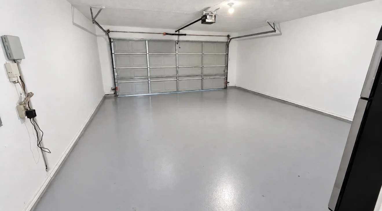 Two car garage with smooth epoxy gray flooring, painted white walls, and an overhead garage door opener.