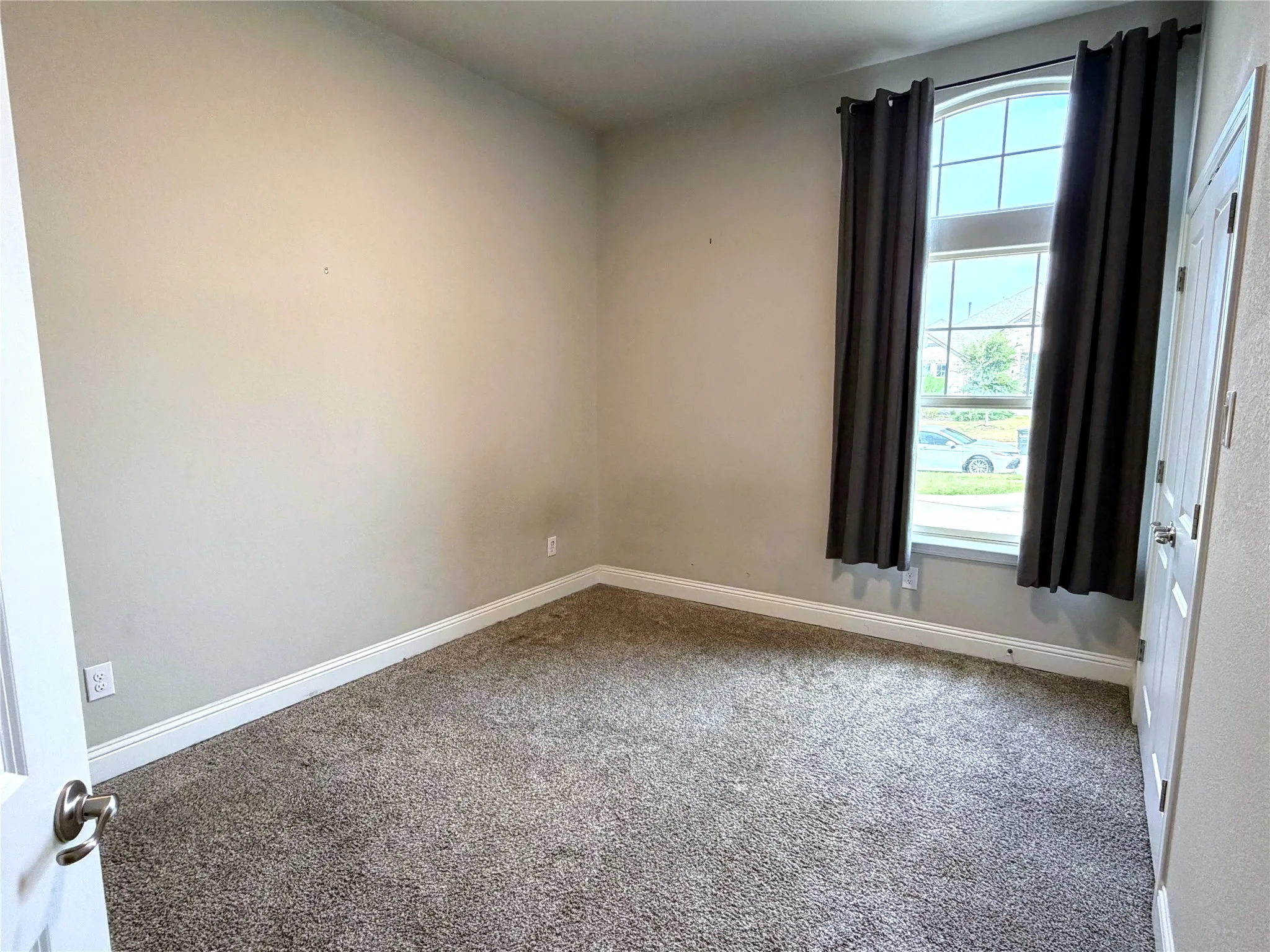 Carpeted interior space featuring neutral wall tones, a tall arched window, and white trim