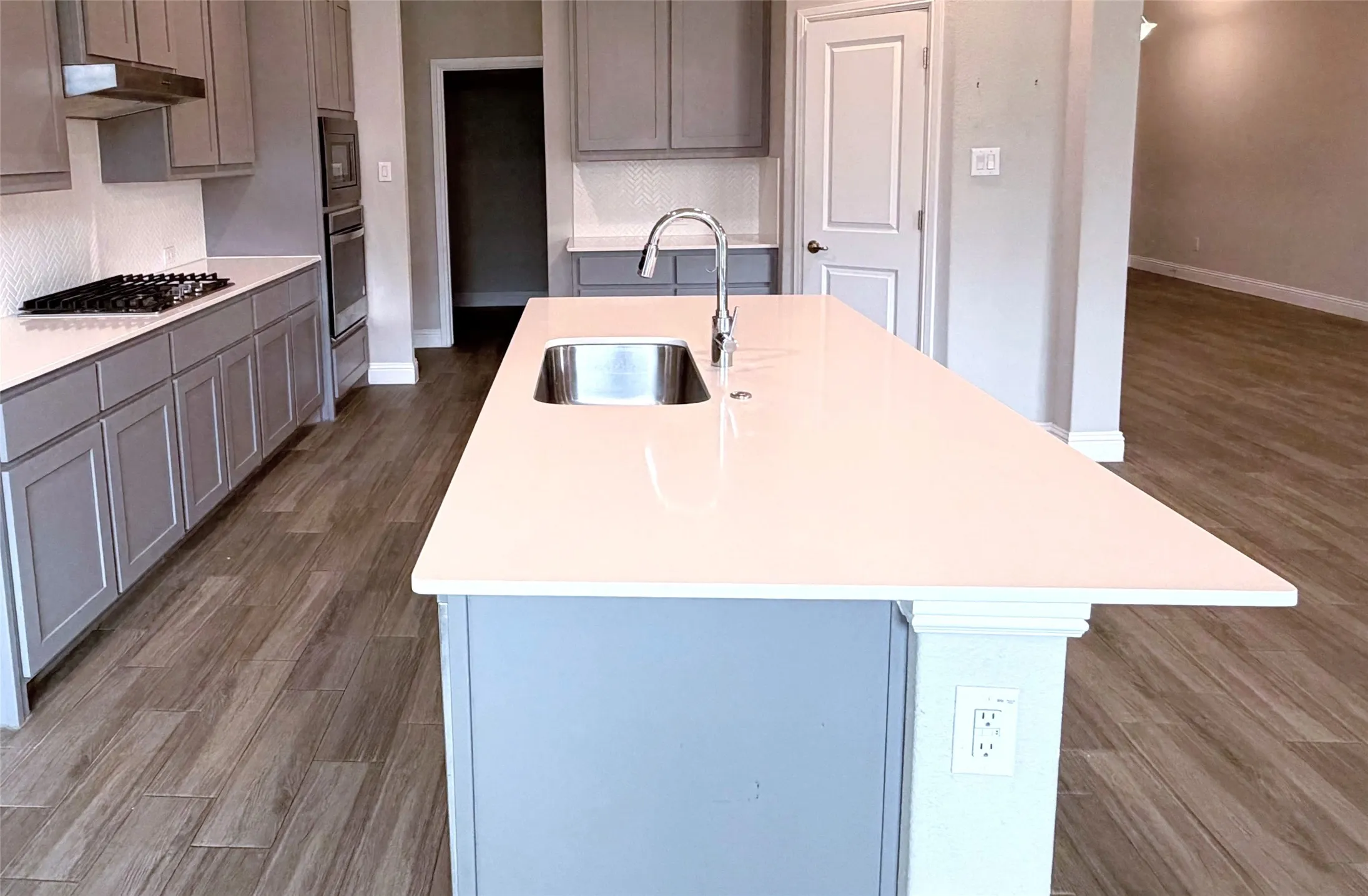 Spacious kitchen island with a built-in sink, gray shaker-style cabinetry, white countertops, stainless steel appliances, and wood-finish flooring