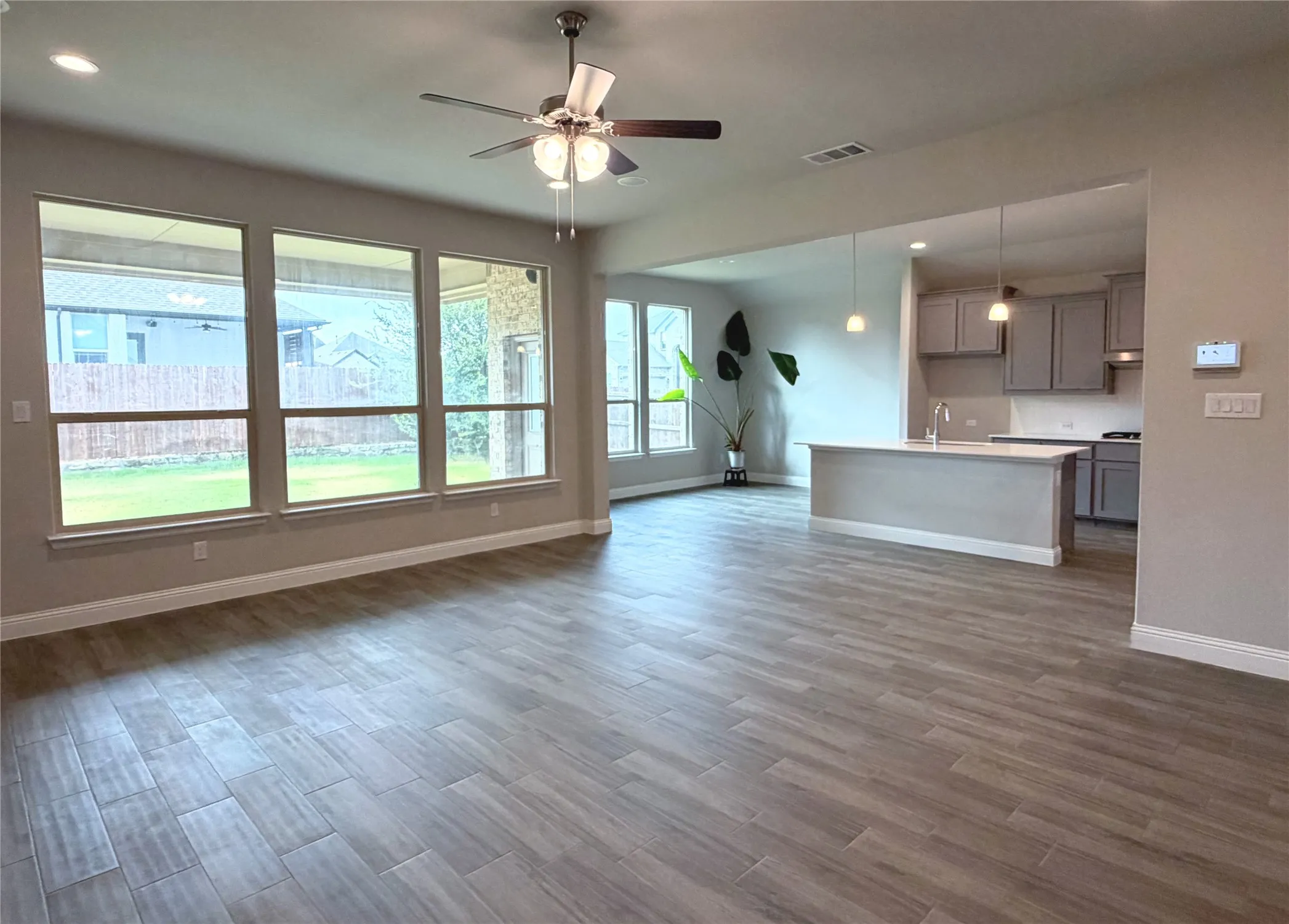 Wood-finish tile flooring throughout, large windows with backyard views, ceiling fan with integrated lighting, kitchen island with seating, and pendant lighting